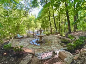 A stone patio with water fountain surrounded by trees.