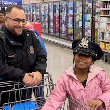 A police officer and girl in pink jacket sitting on shopping cart.