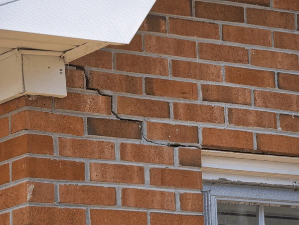 A brick wall with cracks in it and a window.