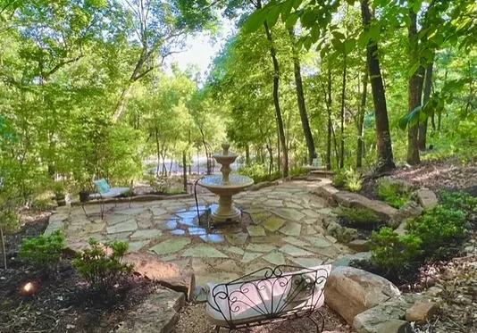 A stone patio with water fountain surrounded by trees.